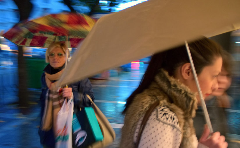 En kvinne og to jenter med paraplyer i regnet.